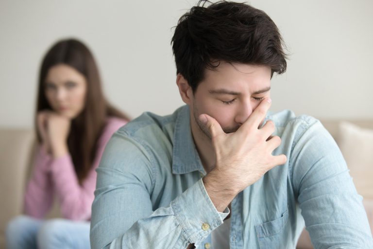 Young Man Stressed With His Hand Over His Face With His Girlfriend Sitting Behind Him Unplanned Pregnancy Advice for Men