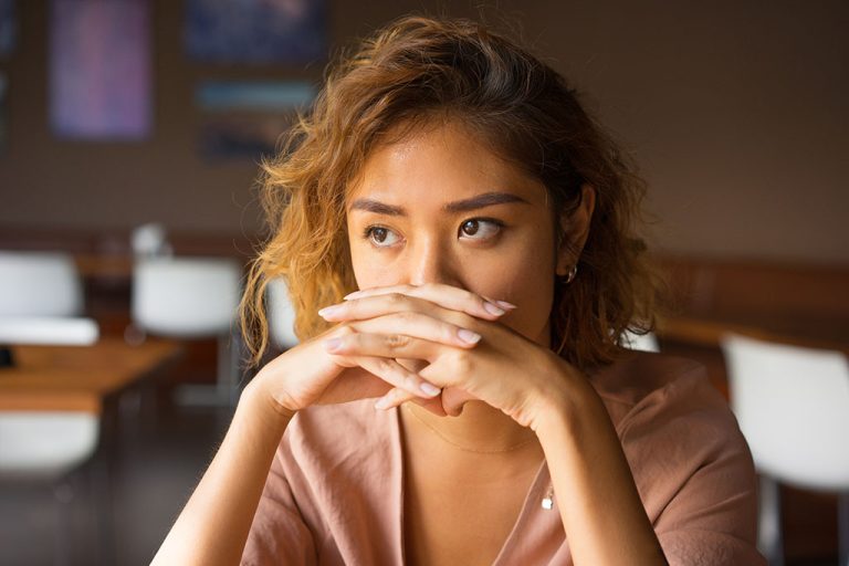 Closeup of a Young Asian Woman Sitting With Her Hands Covering Her Mouth in Deep Thought Regret After Abortion