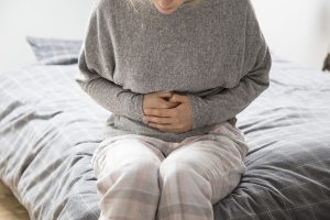 Closeup of a Woman Sitting on a Bed Holding Her Abdomen in Pain Experiencing Bleeding After a Medical Abortion